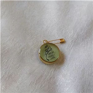 سنجاق سینه رزینی شبتاب سبز مزین به وان یکاد و حرز صغیر امام جواد(ع) قاب برنج طلایی دو سانتی